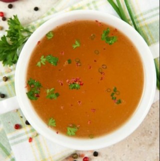 a foto mostra um xicara de sopa com duas abas, vista de cima, com um caldo fino e dourado. Esta salpicado cheiro verde